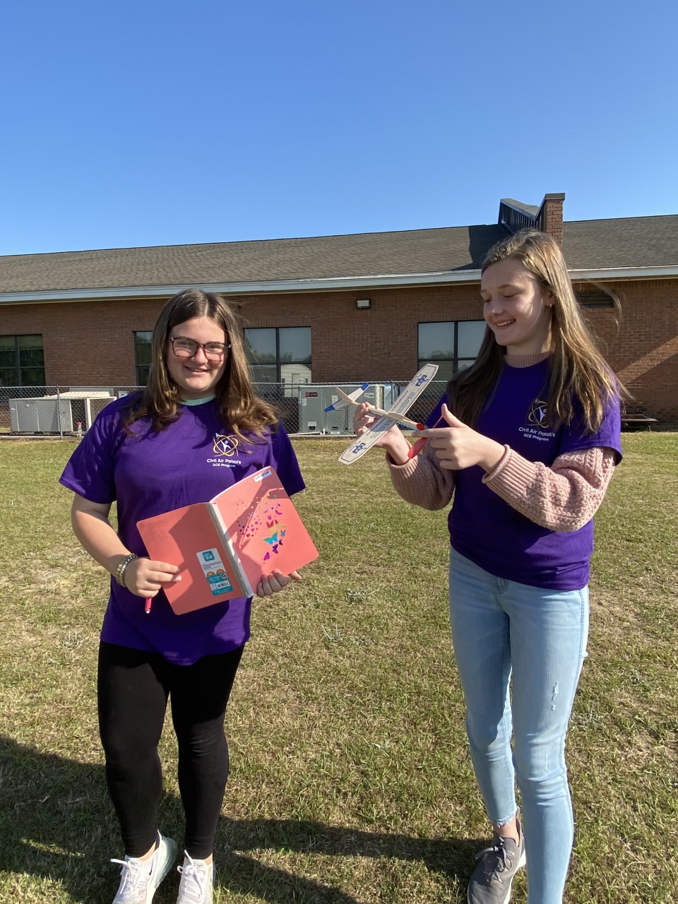 Two students are outside the school preparing to fly their balsa model airplanes