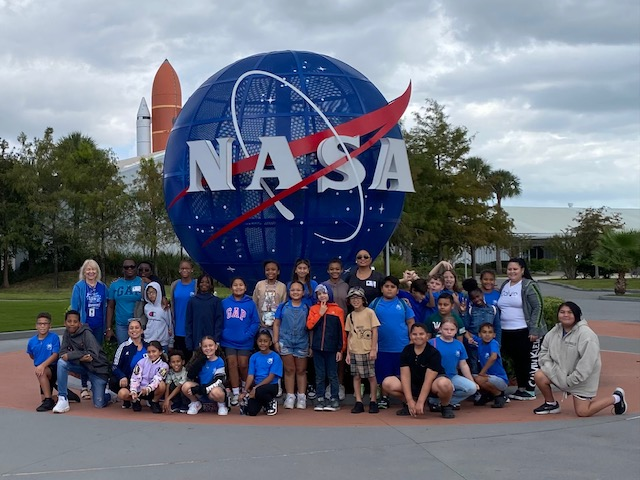 Barbara Walters-Phillips poses at Kennedy Space center in front of the NASA sign with her class